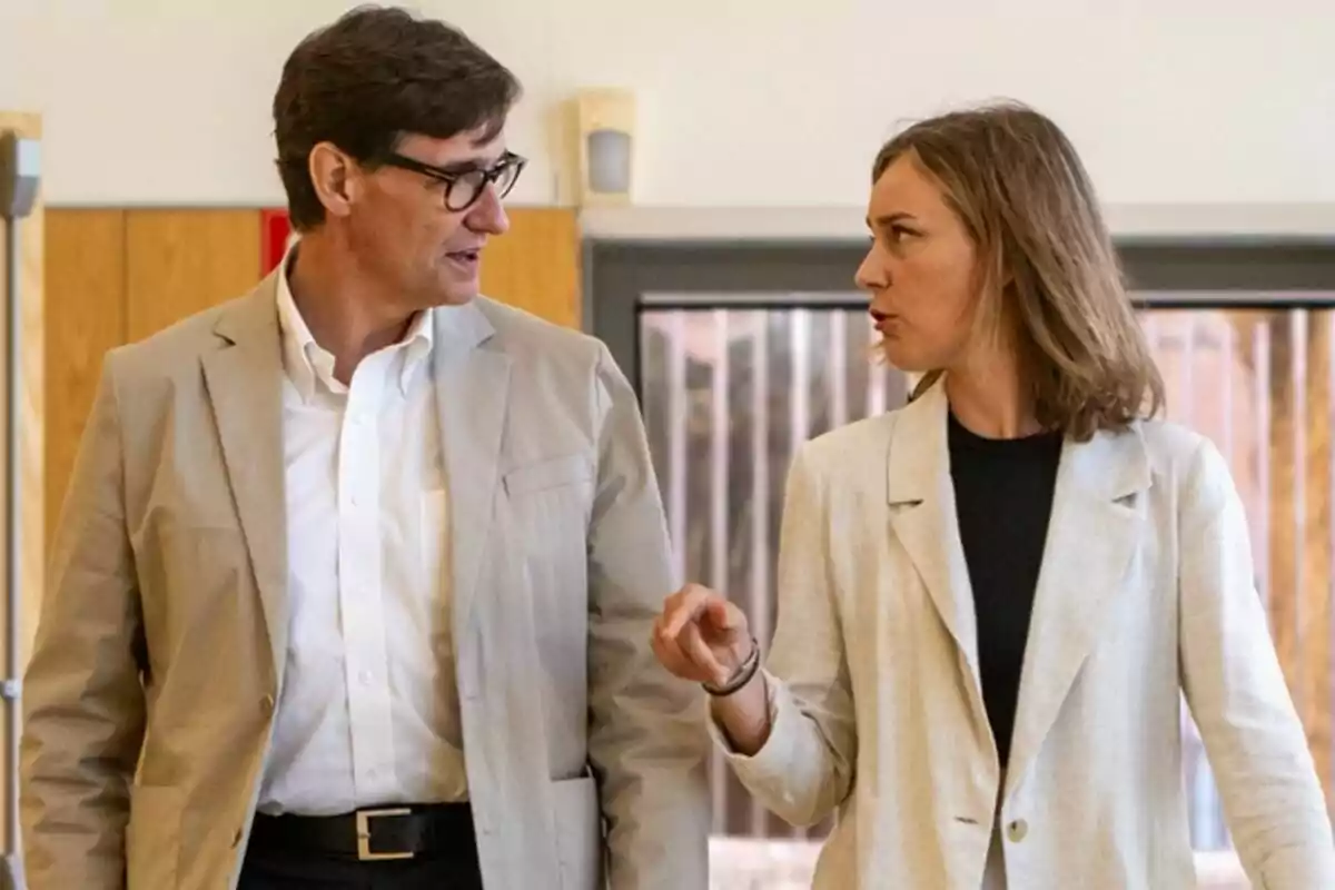 Dues persones conversant mentre caminen en un interior amb parets de fusta.