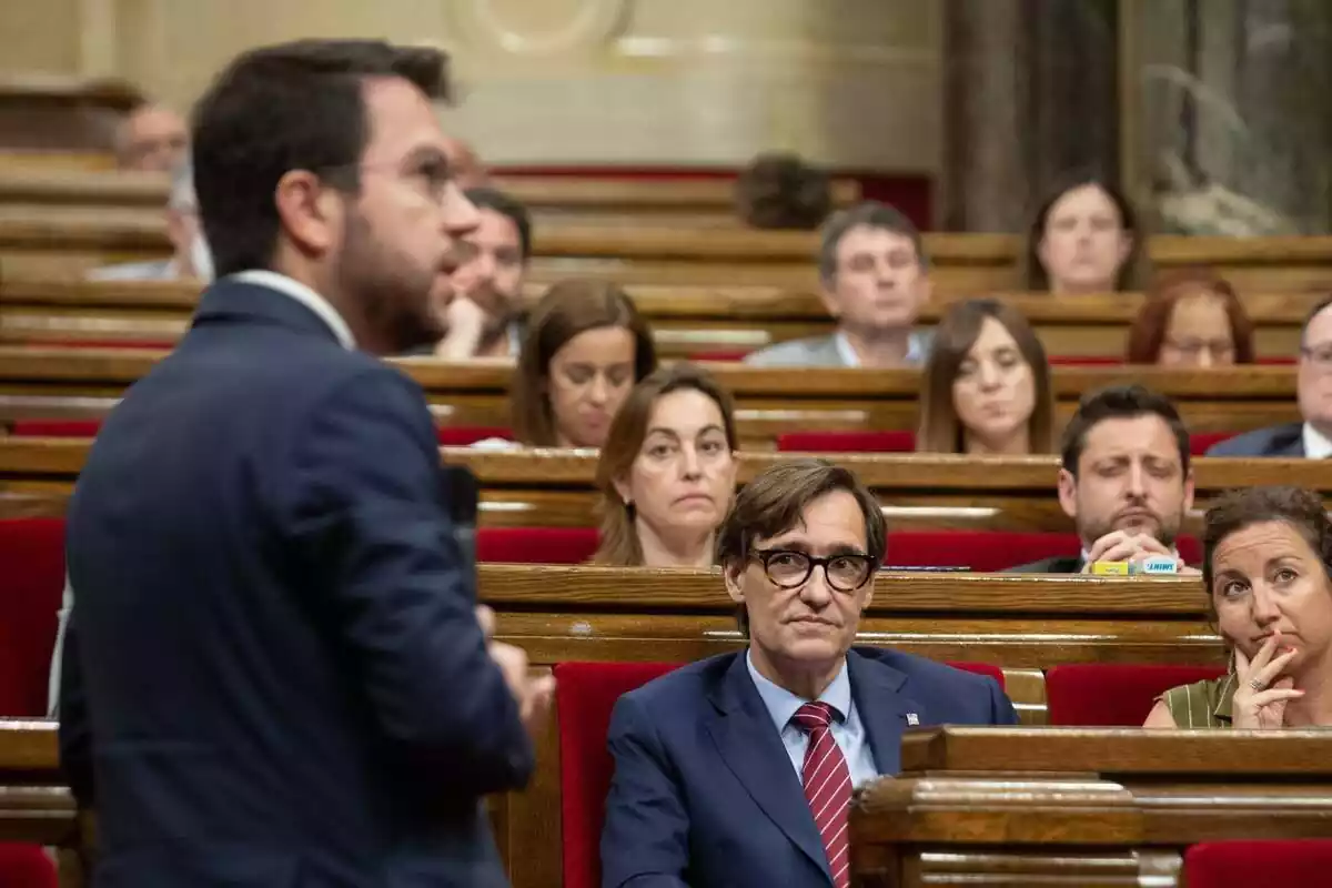 Salvador Illa, en un segon pla, mira atentament Pere Aragonès, en primer pla, mentre aquest parla des del seu escó al Parlament