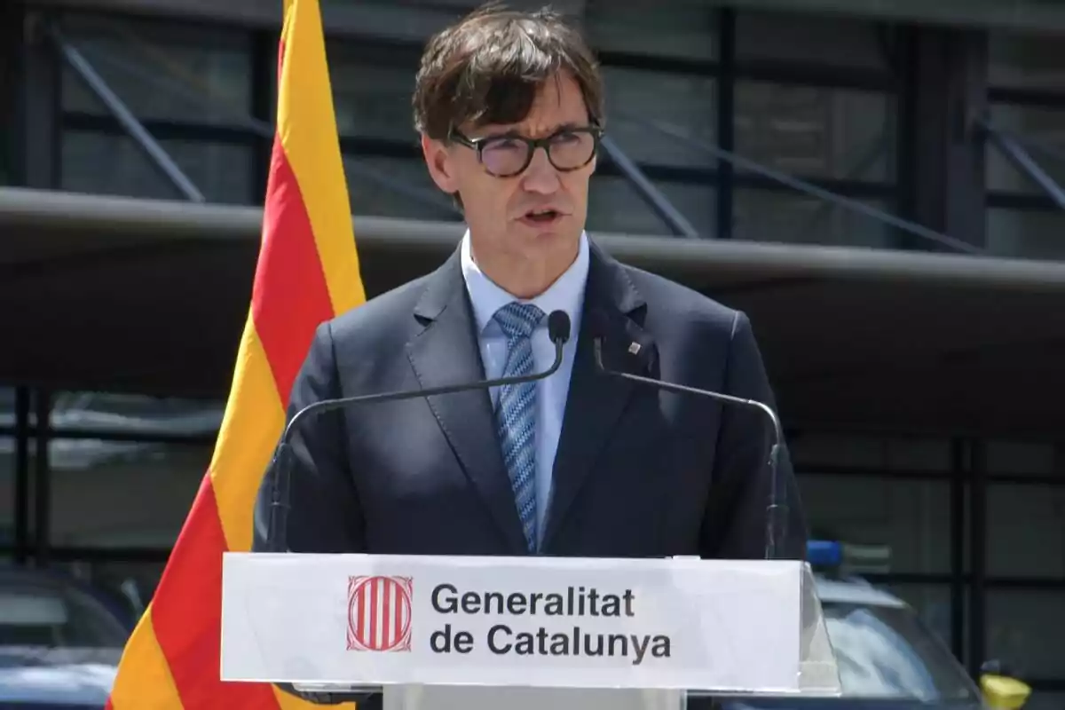 Salvador Illa en un podi amb el logotip de la Generalitat de Catalunya i una bandera catalana de fons.