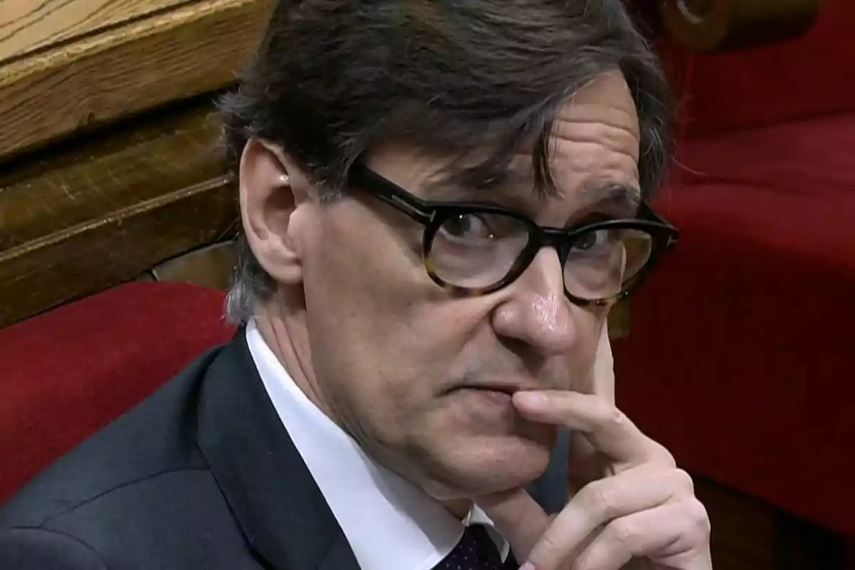 Home amb ulleres de pasta fosques assegut en un banc vermell, mirant pensatiu cap a la càmera i recolzant la mà al rostre