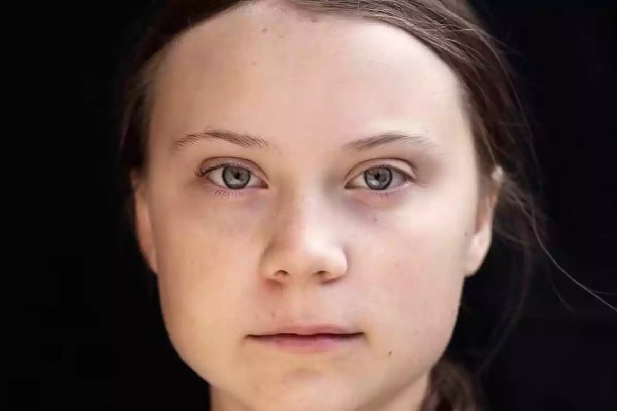 Close-up of a young woman with brown hair and light eyes with a serious expression against a black background