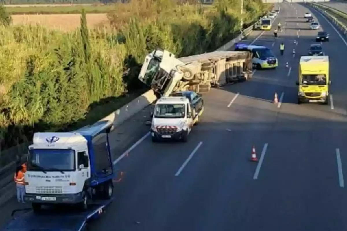 Un camió bolcat en una autopista amb diversos vehicles d?assistència i senyalització de trànsit presents.