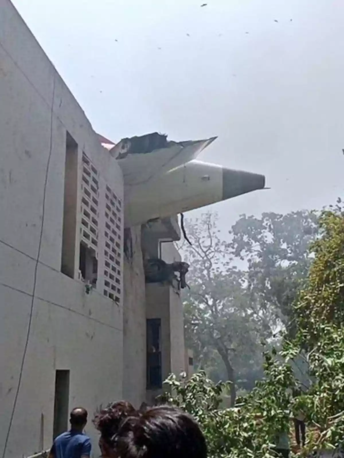 Un avió s’ha estavellat contra un edifici i part de l’aeronau sobresurt de l’estructura mentre diverses persones observen des de baix. Un avió s’ha estavellat contra un edifici i part de l’aeronau sobresurt de l’estructura mentre diverses persones observen des de baix.