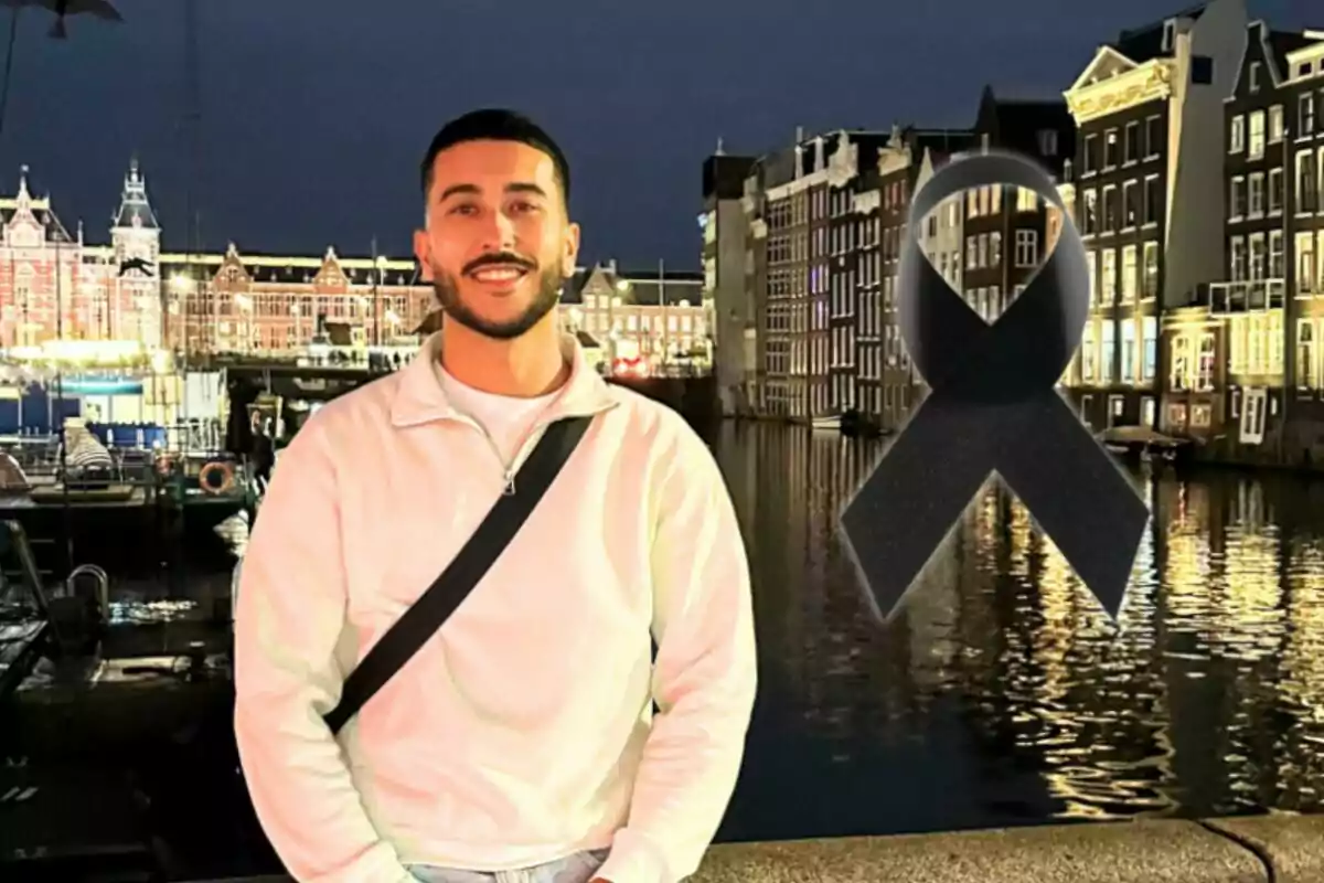 Un home somrient amb barba i jersei clar posa davant d'un canal il·luminat a la nit amb un llaç negre superposat a la imatge.