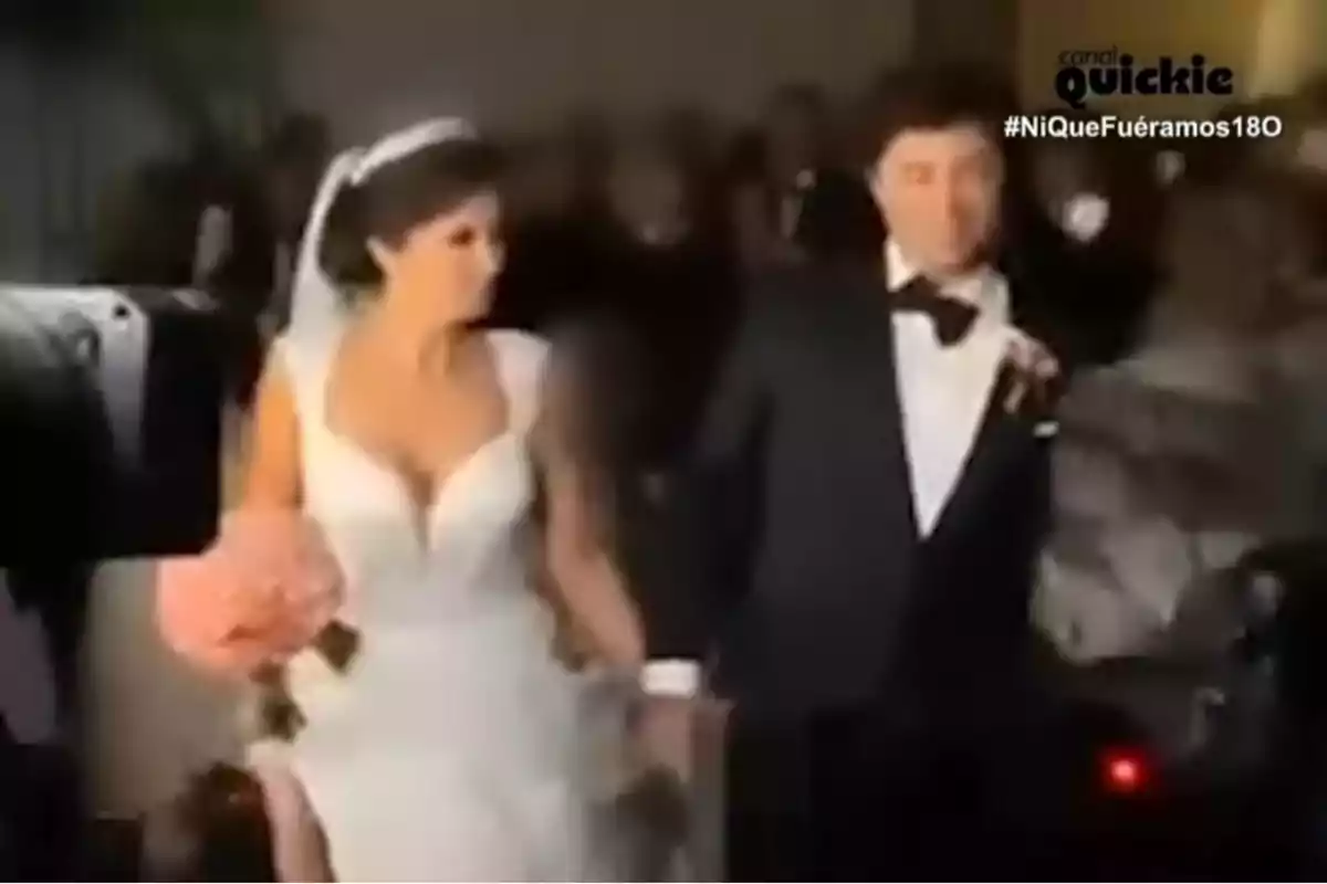 Una parella vestida de Novios camina de la mà en un esdeveniment formal.