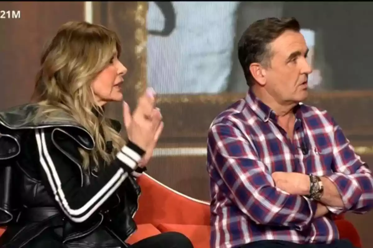Dues persones estan assegudes en un programa de televisió, una dona amb jaqueta negra i ratlles blanques gesticula mentre un home amb camisa de quadres l'escolta amb els braços creuats. Dues persones estan assegudes en un programa de televisió, una dona amb jaqueta negra i ratlles blanques gesticula mentre un home amb camisa de quadres l'escolta amb els braços creuats.