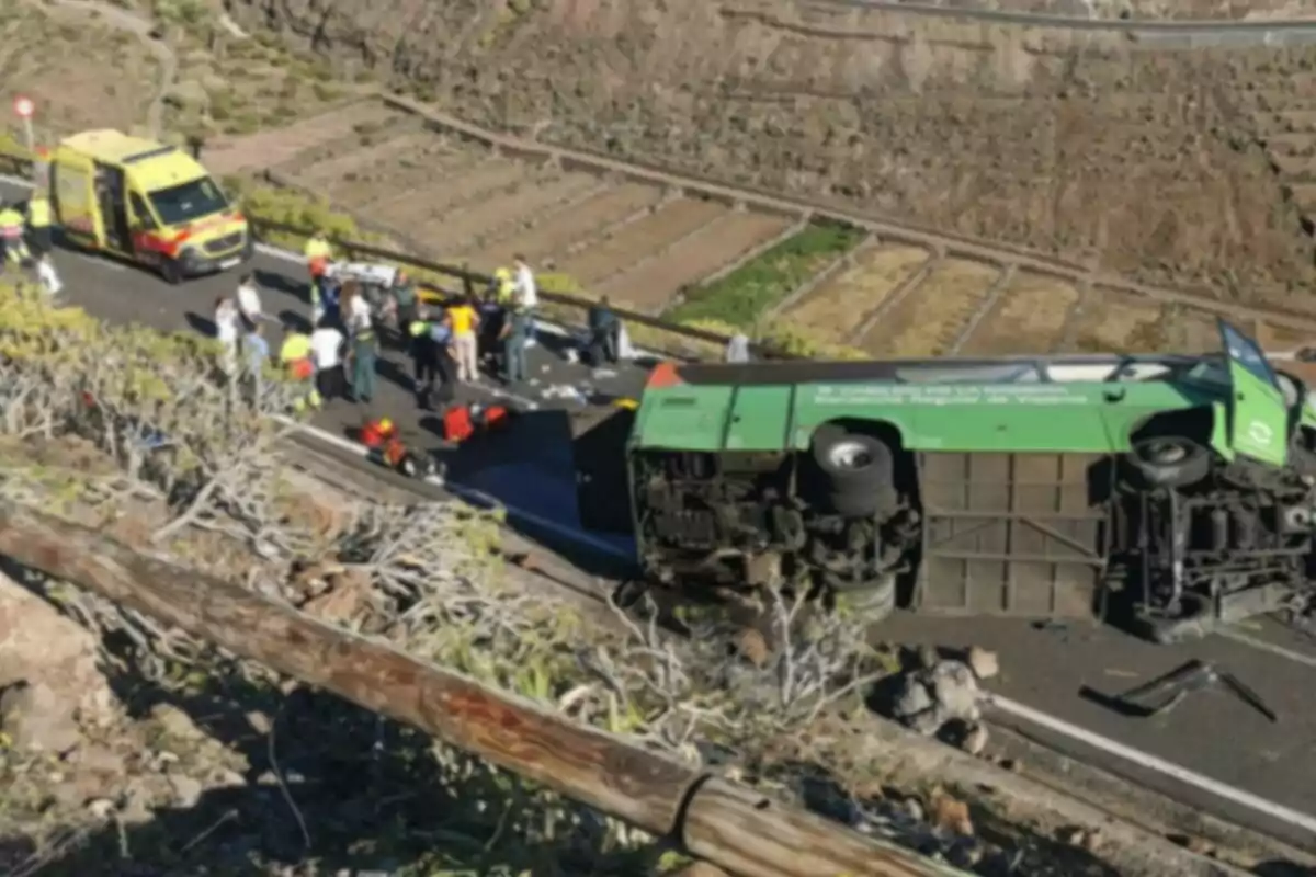 Un autobús bolcat en una carretera de muntanya amb una ambulància i diverses persones al voltant. Un autobús bolcat en una carretera de muntanya amb una ambulància i diverses persones al voltant.