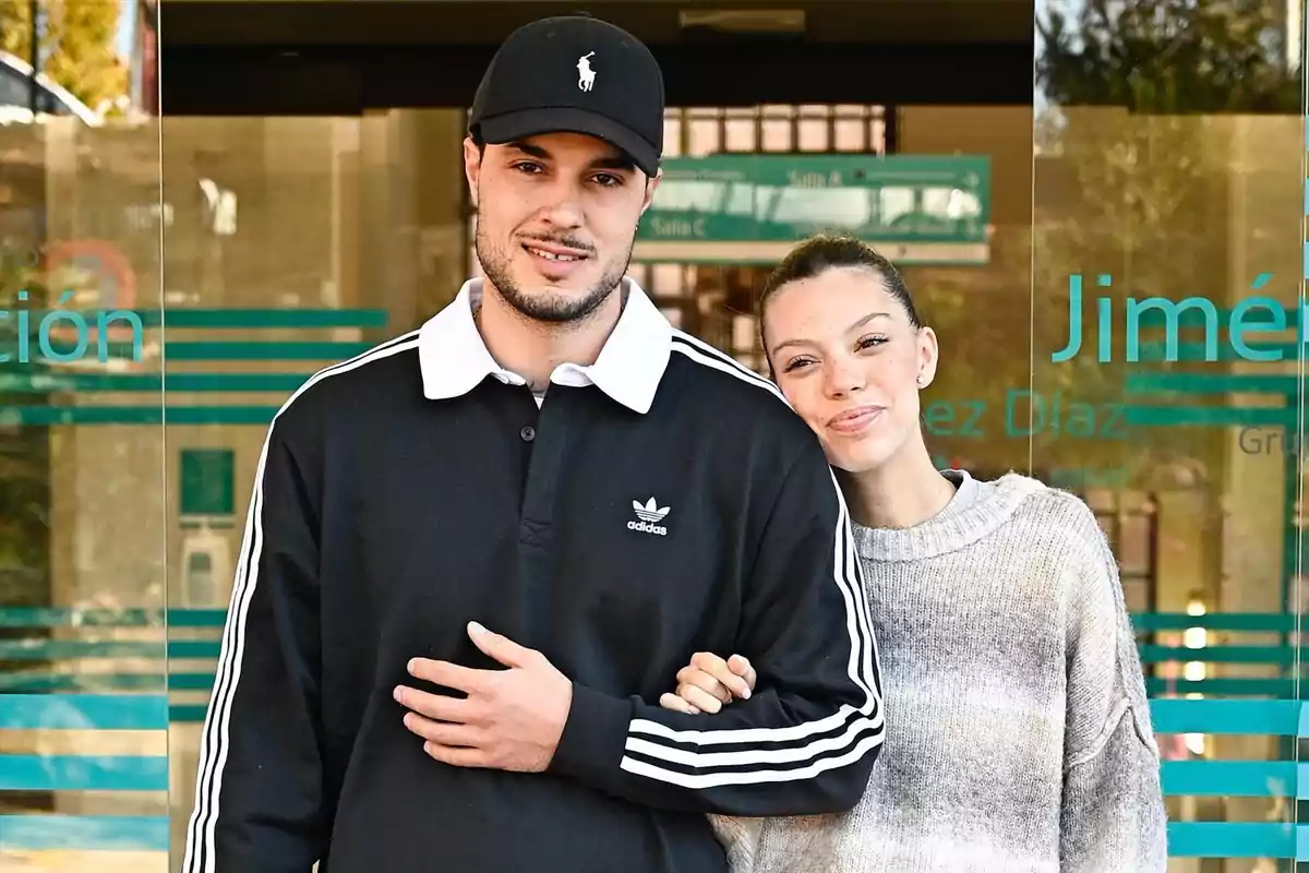 Carlo Costanzia y Alejandra Rubio sonriente posando frente a un edificio con puertas de vidrio.