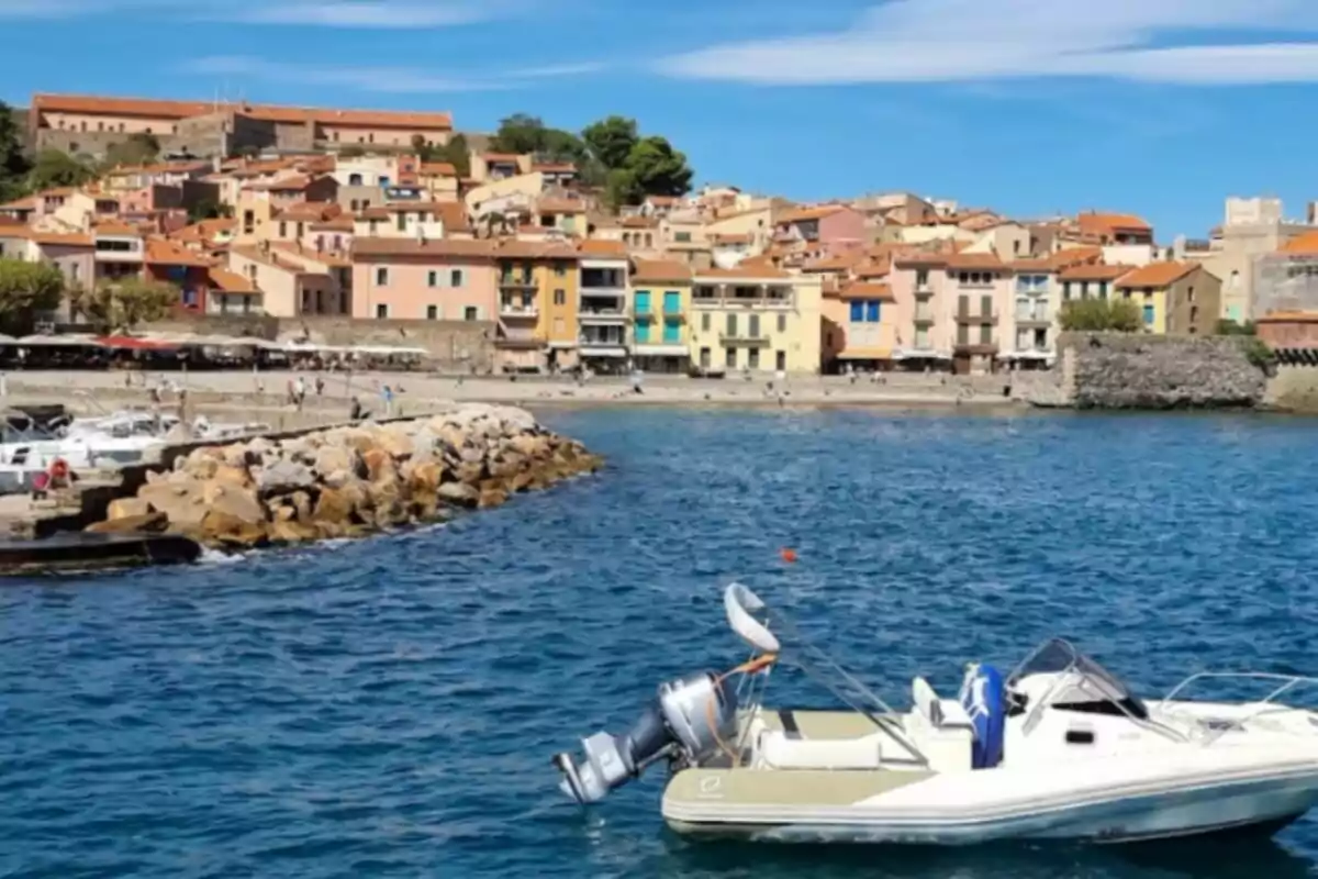 Vista d'un pintoresc poble costaner, Collioure, amb cases acolorides, un moll de roques i un pot a l'aigua.