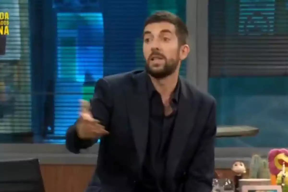 Un home amb barba i vestit fosc gesticula mentre parla en un programa de televisió.