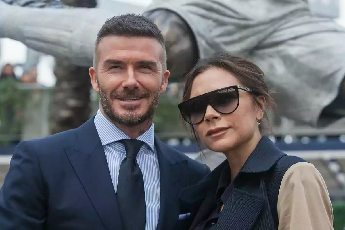 David Beckham y Victoria Beckham posando juntos, él lleva traje y corbata, ella lleva gafas de sol grandes.