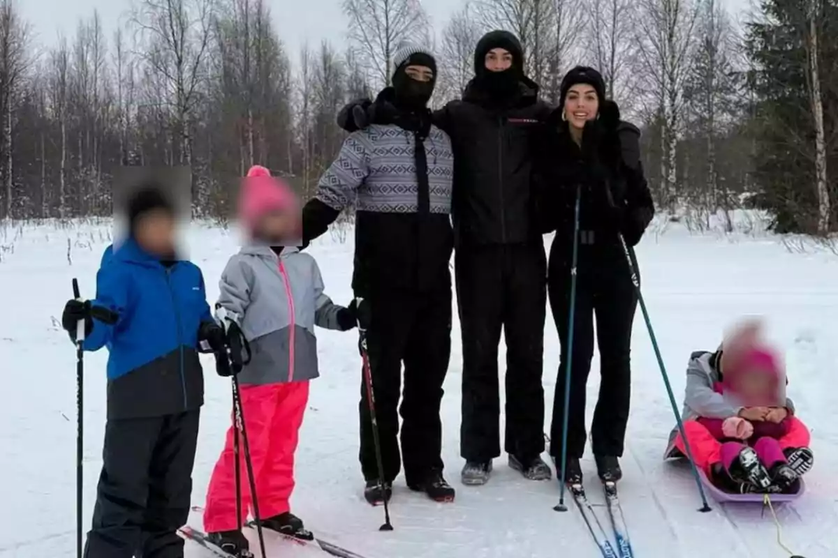 A group of people dressed in winter clothing is enjoying an outdoor activity in the snow, some are standing with skis and poles while others are sitting on a sled, surrounded by leafless trees. A group of people dressed in winter clothing is enjoying an outdoor activity in the snow, some are standing with skis and poles while others are sitting on a sled, surrounded by leafless trees.