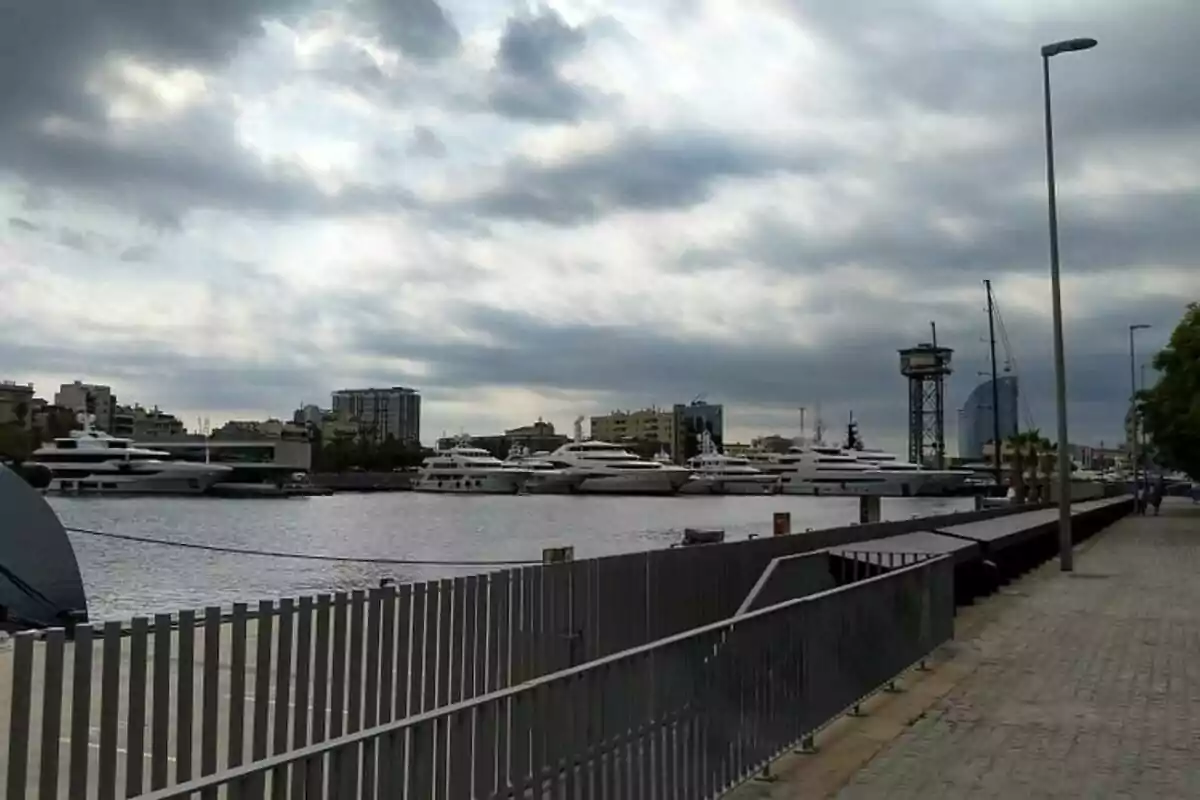 Vista del puerto de Barcelona con varios yates amarrados y un cielo nublado.