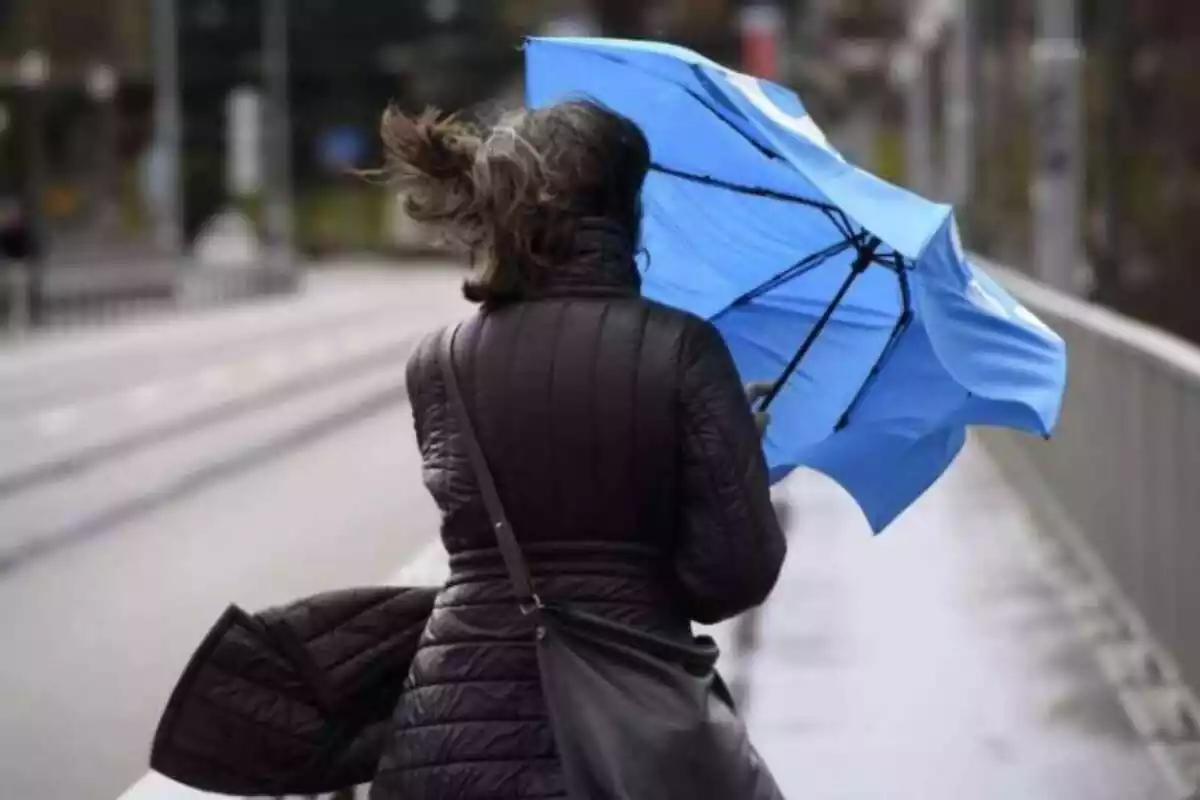 Dona subjectant un paraigua enmig d'un temporal de pluja i vent