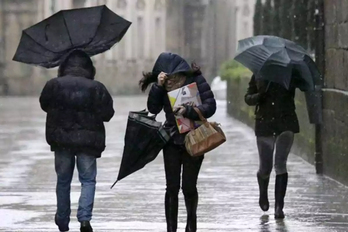 Persones amb paraigües caminant pel carrer mentre fa un temporal de pluja i vent