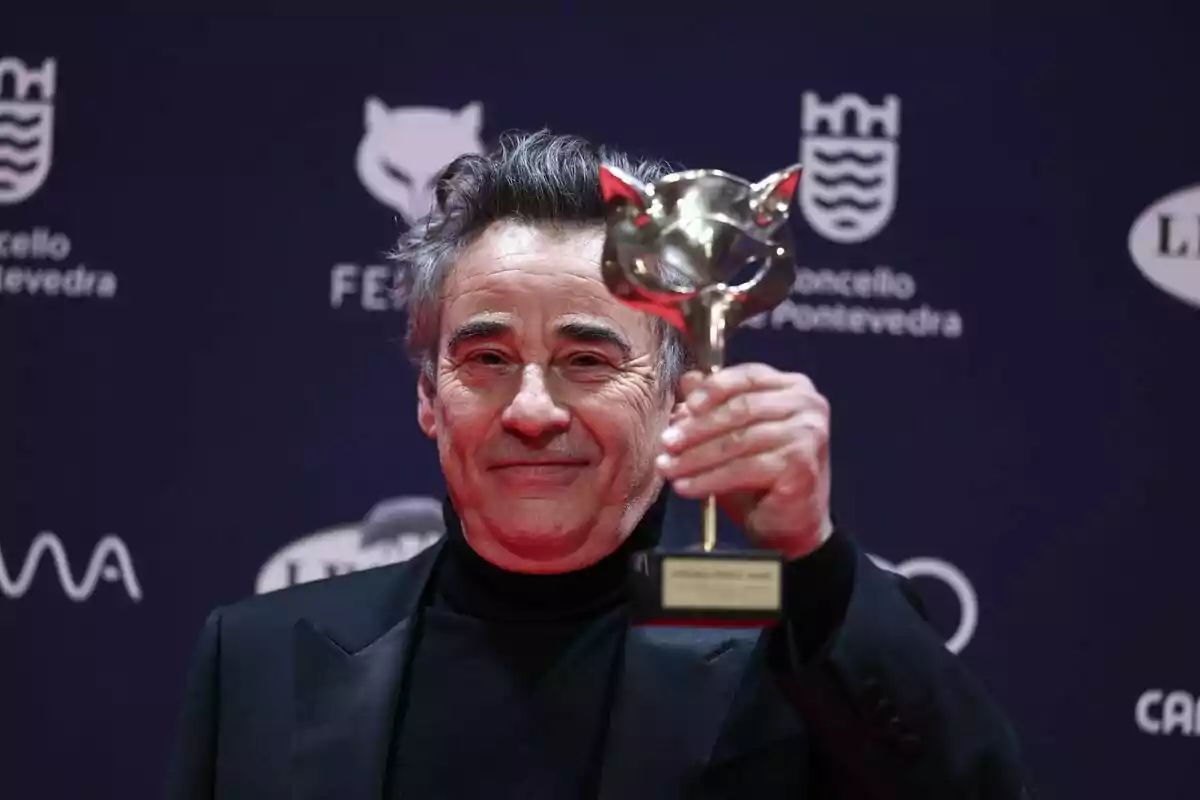 A man holding a trophy at an event with a background of logos. A man holding a trophy at an event with a background of logos.
