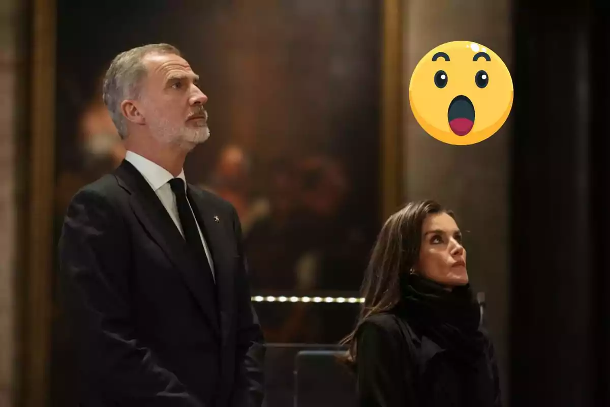 Dues persones vestides de negre mirant cap amunt amb una expressió de sorpresa representada per un emoji.