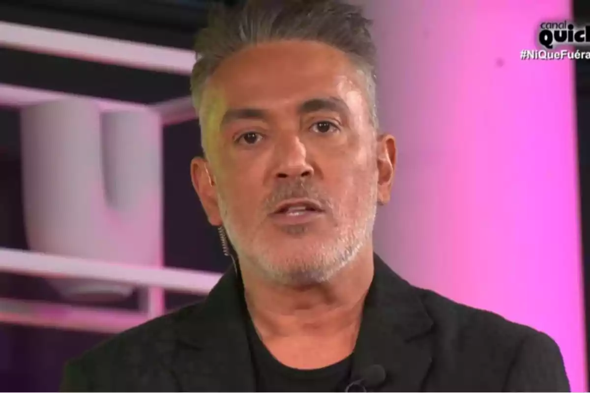 Kiko Hernández con cabello canoso y barba está hablando en un programa de televisión con un fondo iluminado en tonos rosados. Kiko Hernández con cabello canoso y barba está hablando en un programa de televisión con un fondo iluminado en tonos rosados.