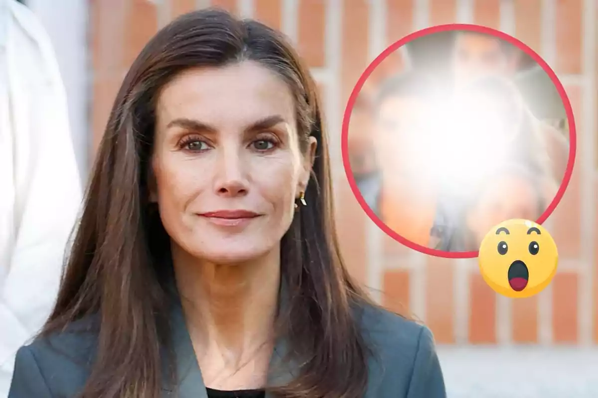 La reina Letizia con cabello oscuro y expresión neutral está frente a un fondo de ladrillos con un círculo borroso y un emoji sorprendido en la esquina.