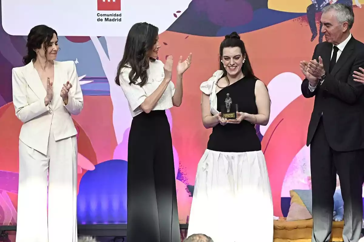 A group of people applauds while a woman holds a trophy at an event with a colorful background and a Comunidad de Madrid sign. A group of people applauds while a woman holds a trophy at an event with a colorful background and a Comunidad de Madrid sign.
