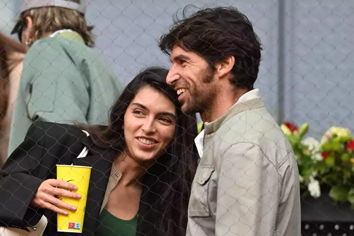 A couple smiles while watching a sporting event behind a net. A couple smiles while watching a sporting event behind a net.