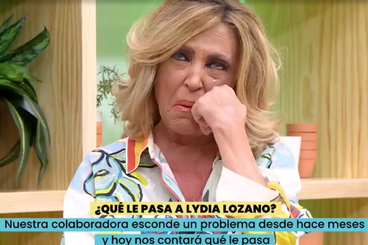 Dona rossa amb expressió trista i llàgrimes als ulls, asseguda en un plató de televisió amb plantes de fons i un text a la pantalla que pregunta què li passa a Lydia Lozano. Dona rossa amb expressió trista i llàgrimes als ulls, asseguda en un plató de televisió amb plantes de fons i un text a la pantalla que pregunta què li passa a Lydia Lozano.
