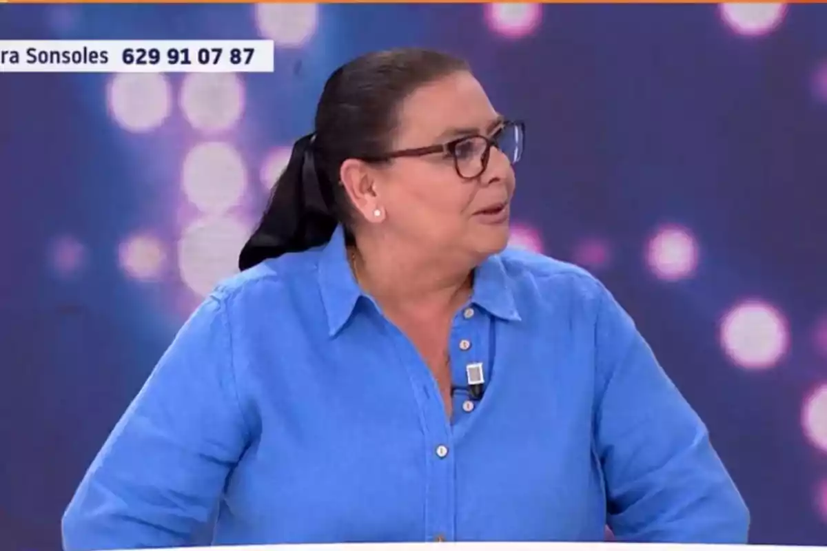 Una persona amb camisa blava i ulleres està participant en un programa de televisió amb un fons de llums desenfocades. Una persona amb camisa blava i ulleres està participant en un programa de televisió amb un fons de llums desenfocades.