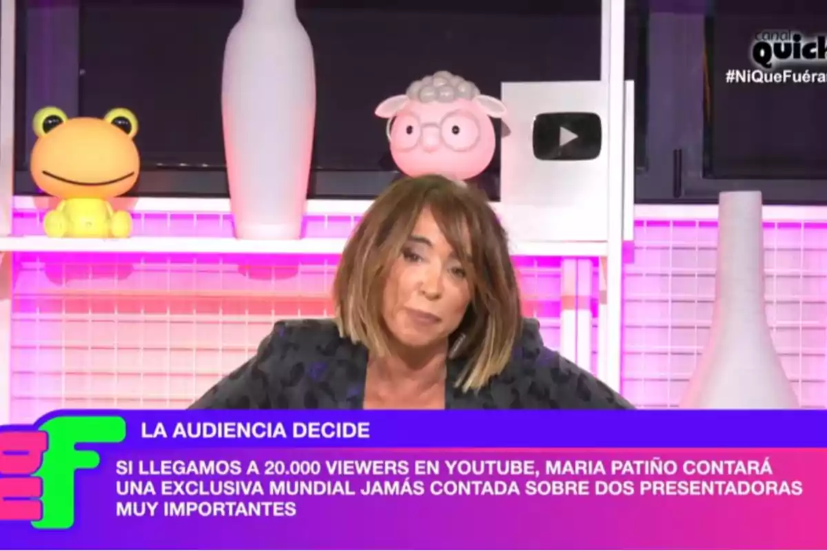 Una presentadora en un set de televisió amb decoracions acolorides i un missatge en pantalla sobre una exclusiva mundial si s'assoleix un número específic d'espectadors a YouTube. Una presentadora en un set de televisió amb decoracions acolorides i un missatge en pantalla sobre una exclusiva mundial si s'assoleix un número específic d'espectadors a YouTube.