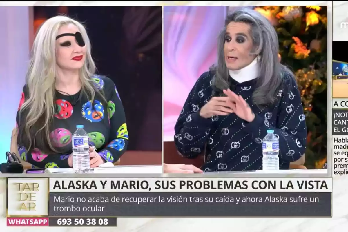 Dues persones assegudes en un programa de televisió, una porta un pegat a l'ull i un vestit amb estampat colorit, mentre que l'altra té el cabell llarg i canós i vesteix un suèter fosc amb patrons clars, ambdues tenen ampolles d'aigua sobre la taula.