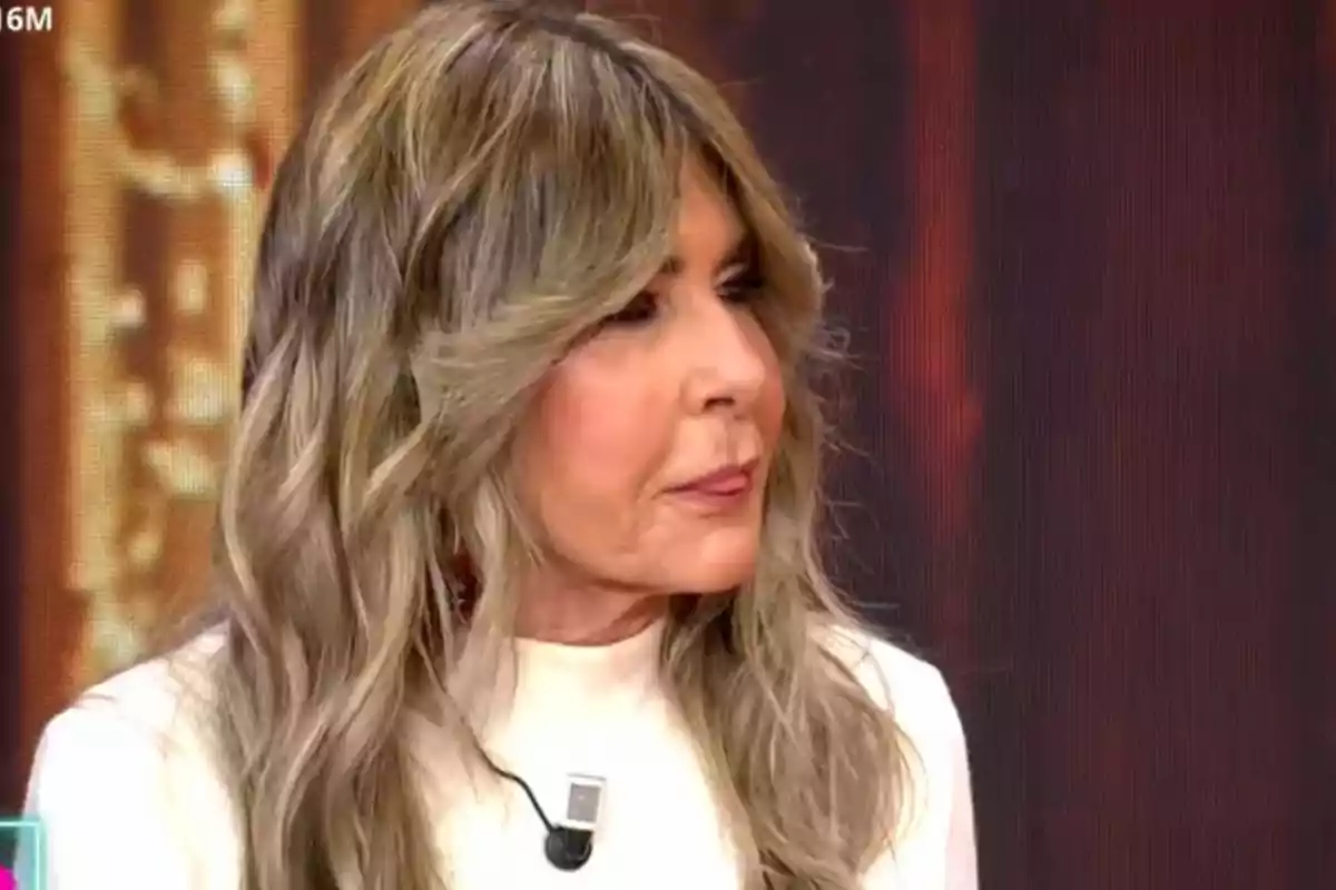 Una persona amb cabell llarg i ros cendra, vestida amb una brusa blanca, està participant en un programa de televisió.