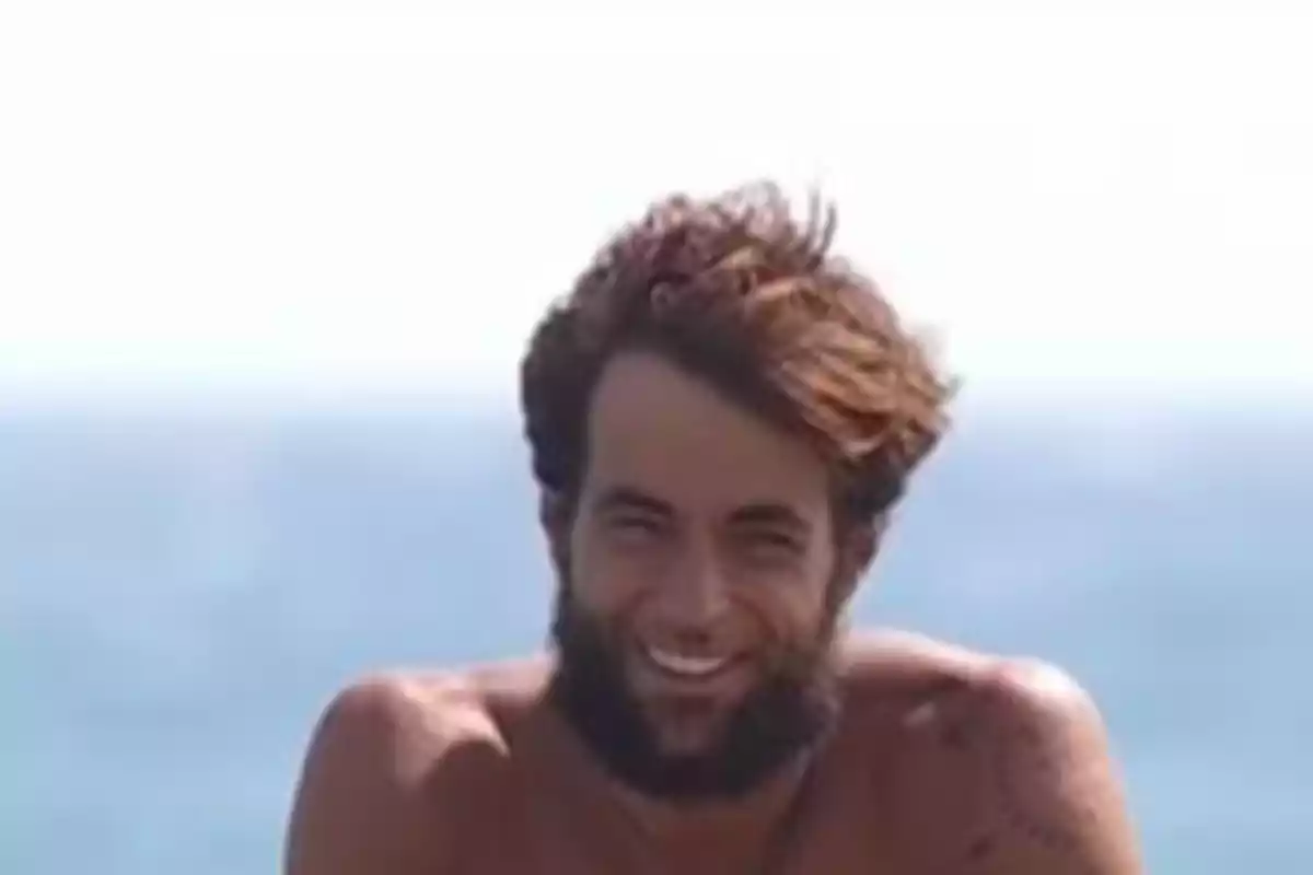 Young man with a beard and messy hair smiling in front of the sea Young man with a beard and messy hair smiling in front of the sea