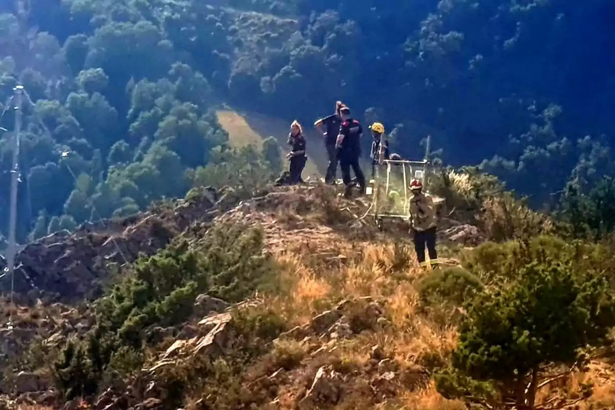 Un grup de rescatistes es troba en una zona muntanyosa fent tasques de rescat, envoltats de vegetació i amb equip especialitzat.