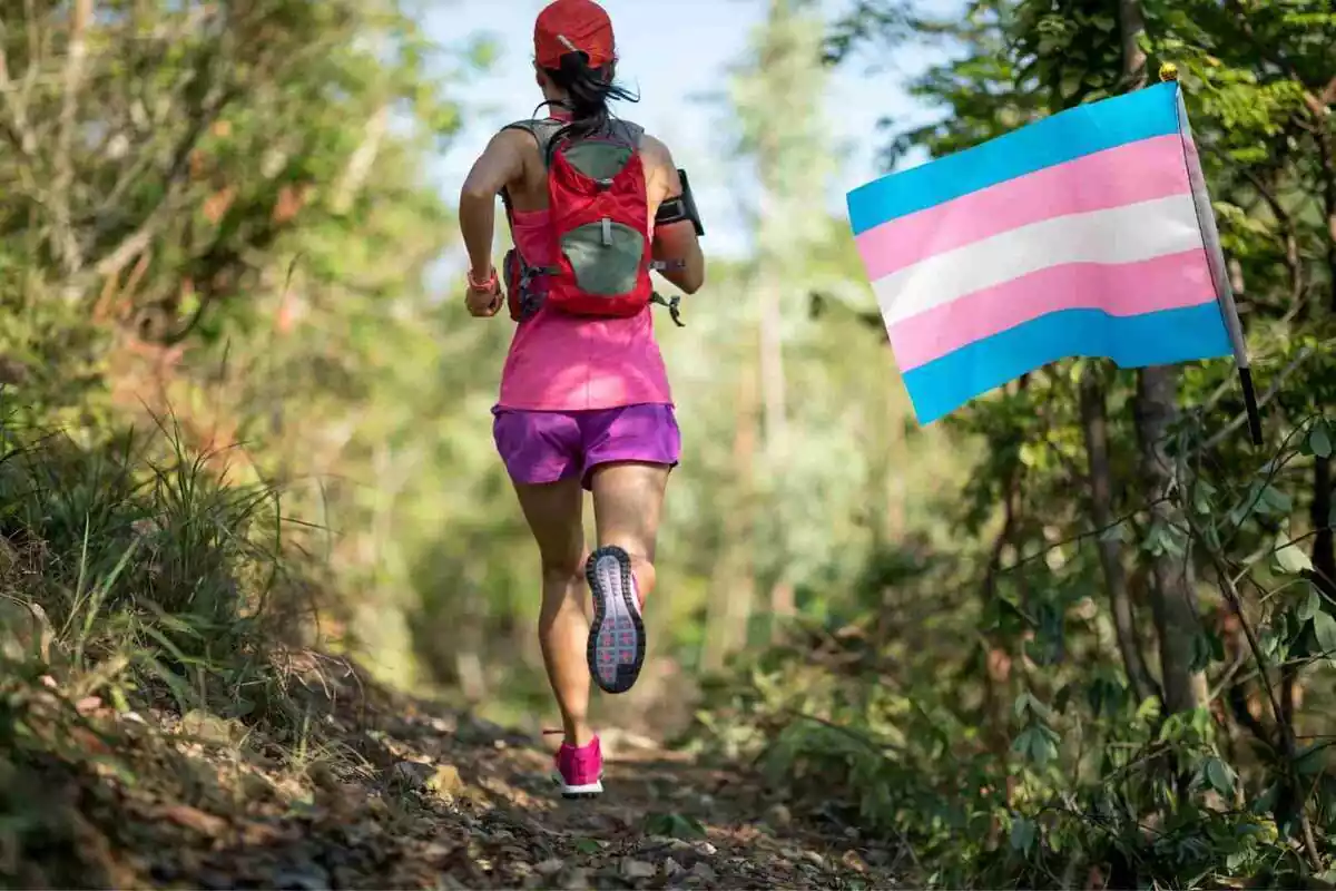 Dona atleta corrent d'esquena al costat d'una bandera del col·lectiu trans