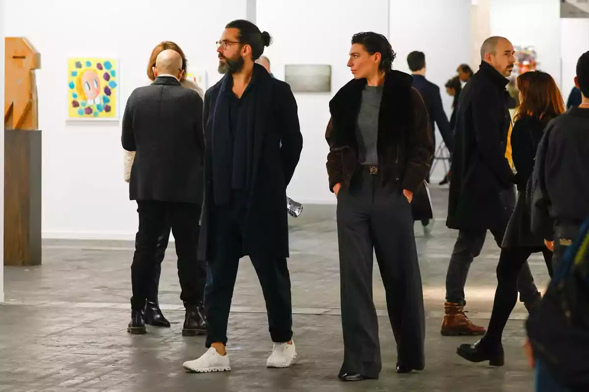 People walking and observing artworks in a gallery, with various paintings and sculptures displayed on the walls and pedestals. People walking and observing artworks in a gallery, with various paintings and sculptures displayed on the walls and pedestals.