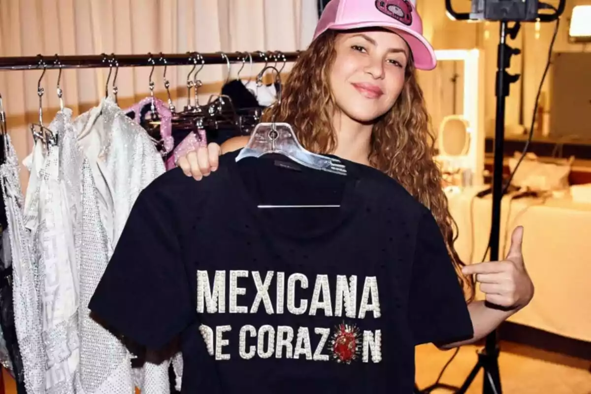A person with a pink cap holds a black T-jersey that says A person with a pink cap holds a black T-jersey that says