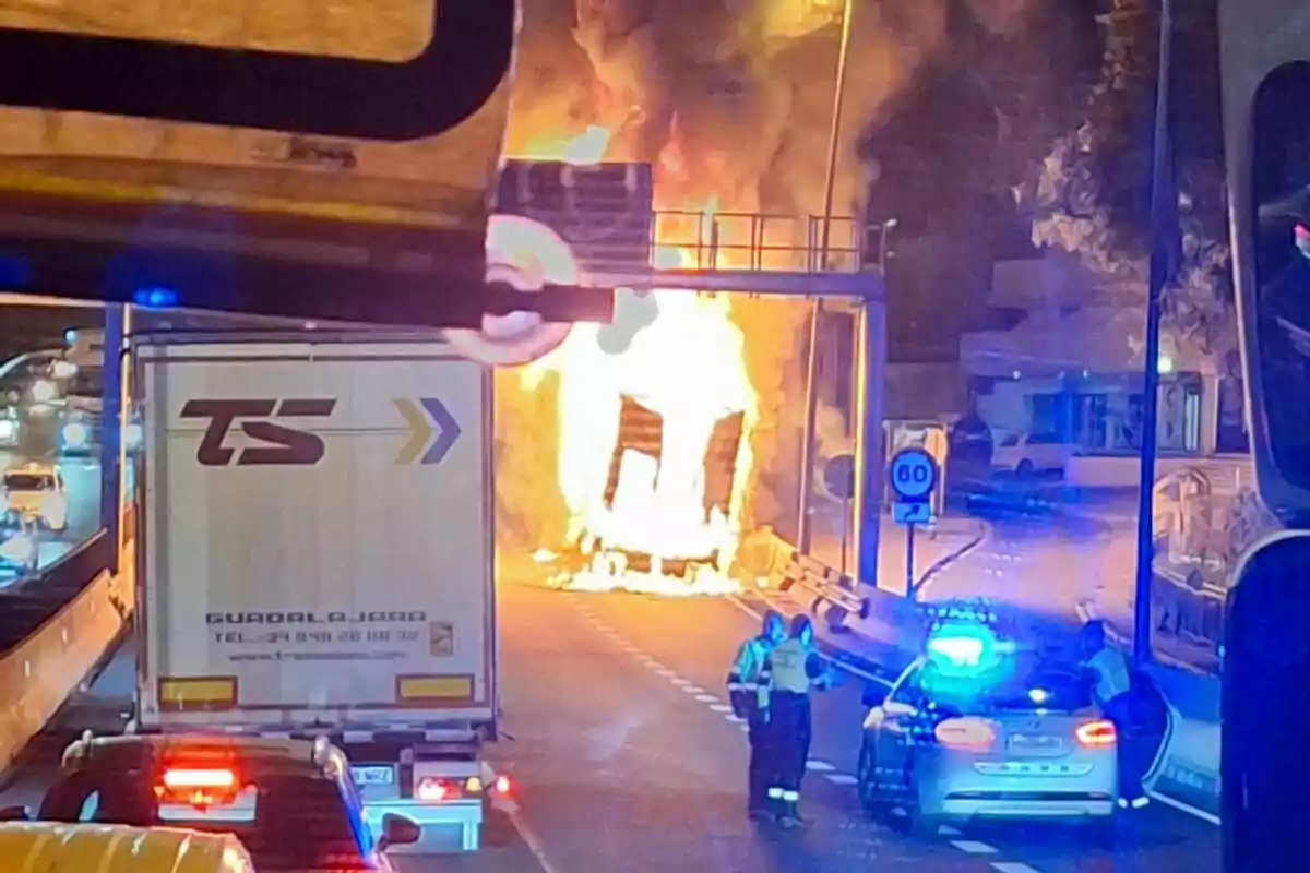 Un camió en flames a una carretera amb presència de vehicles d'emergència i trànsit detingut.