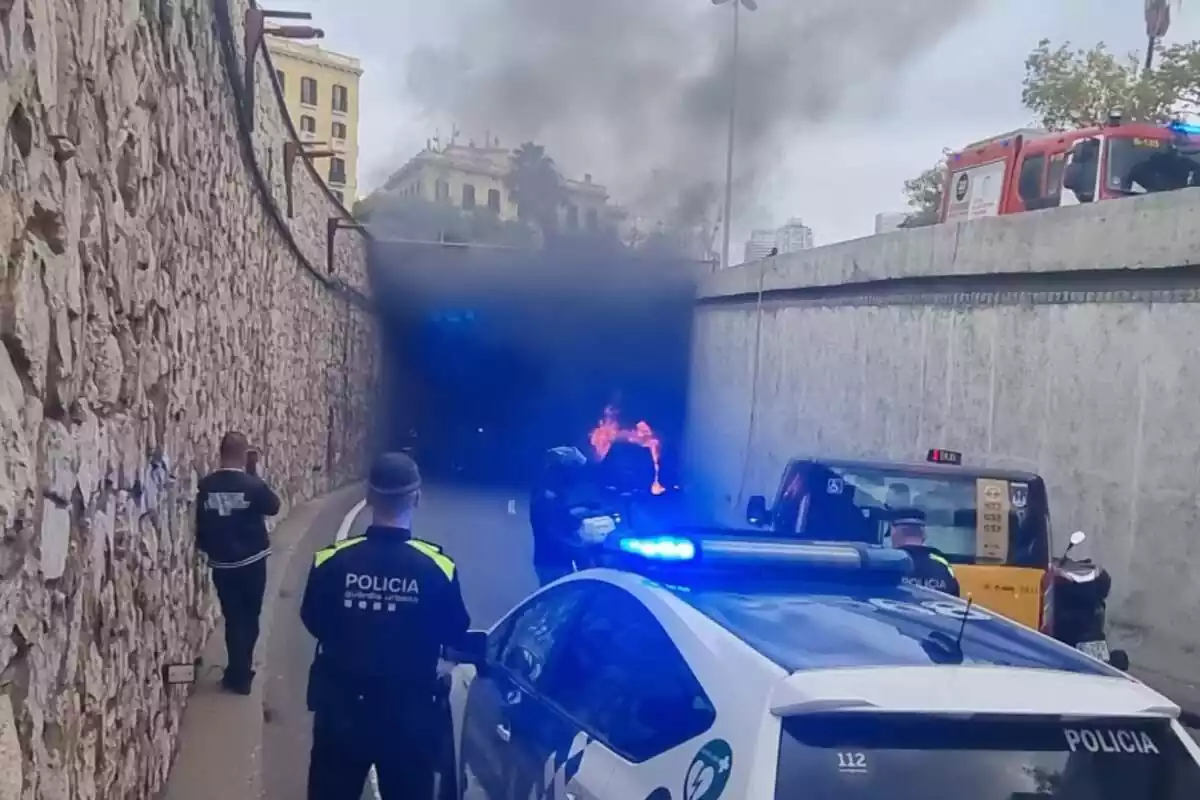 Imatge ed un cotxe incendiat a la Ronda Litoral de Barcelona mentre agents de la Guàrdia Urbana intervenen a l'incident