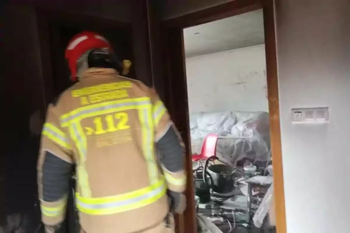 Un bombero con casco rojo inspecciona una habitación desordenada.