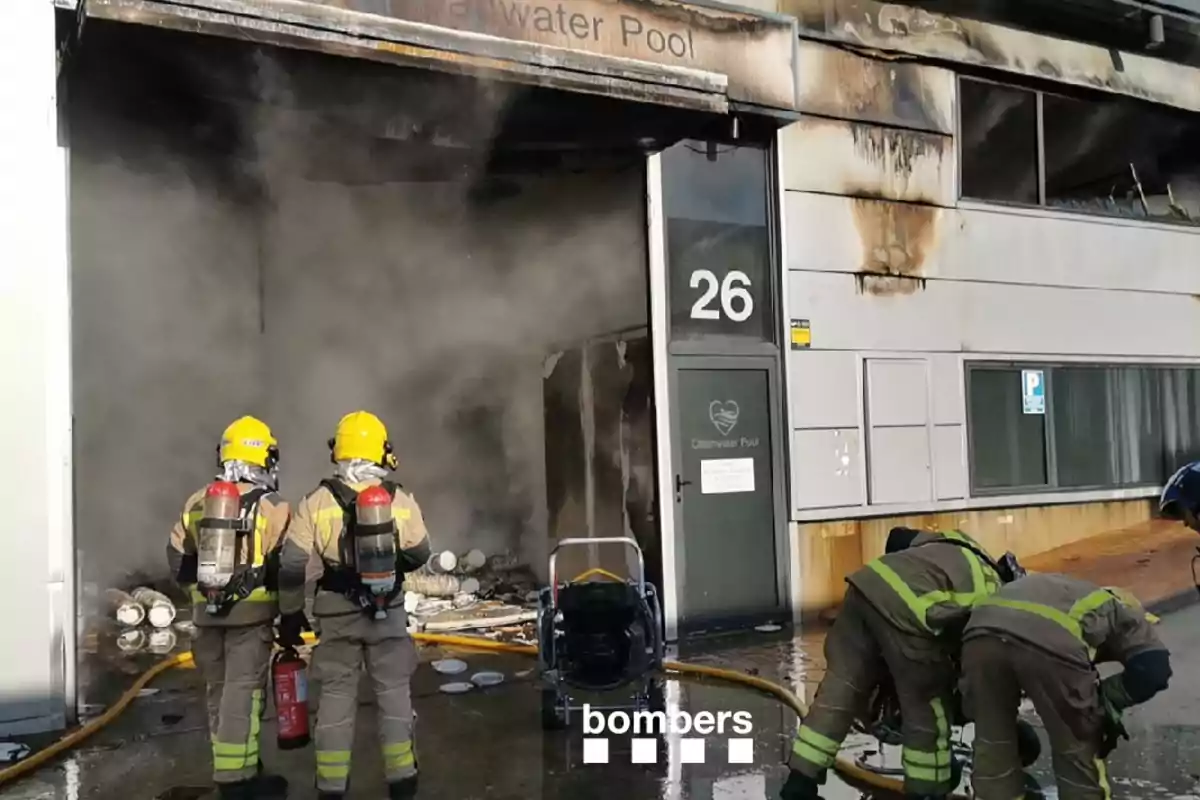 Bombers treballant per controlar un incendi en un edifici industrial mentre el fum surt per la porta. Bombers treballant per controlar un incendi en un edifici industrial mentre el fum surt per la porta.