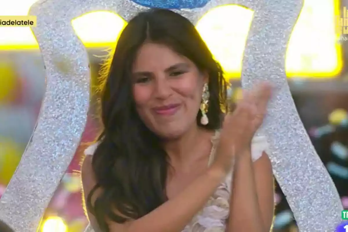 Isa Pantoja amb cabell fosc i llarg aplaudeix mentre somriu, amb un fons acolorit i brillant a l'estrena de La Família de la Tele.