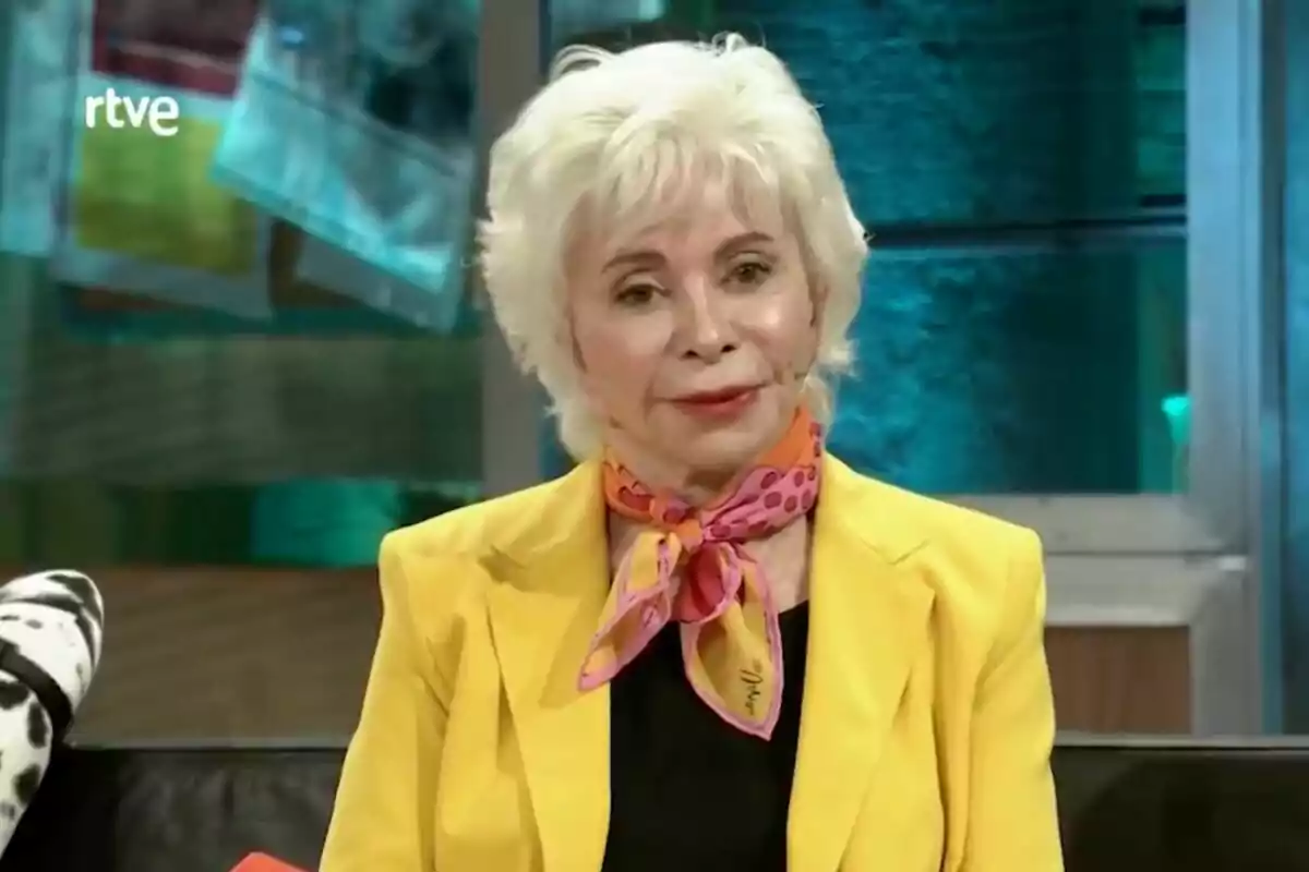 Isabel Allende amb cabell blanc i curt porta un mocador acolorit i una jaqueta groga mentre està asseguda a 'La Revuelta'.