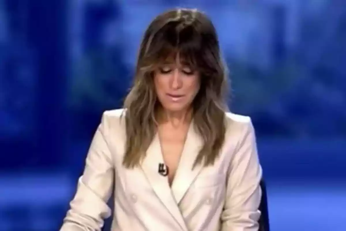 Isabel Jiménez emocionada amb cabells llargs i solts, vestida amb un blazer clar, al plató d'Informativos telecinco amb un fons blau.