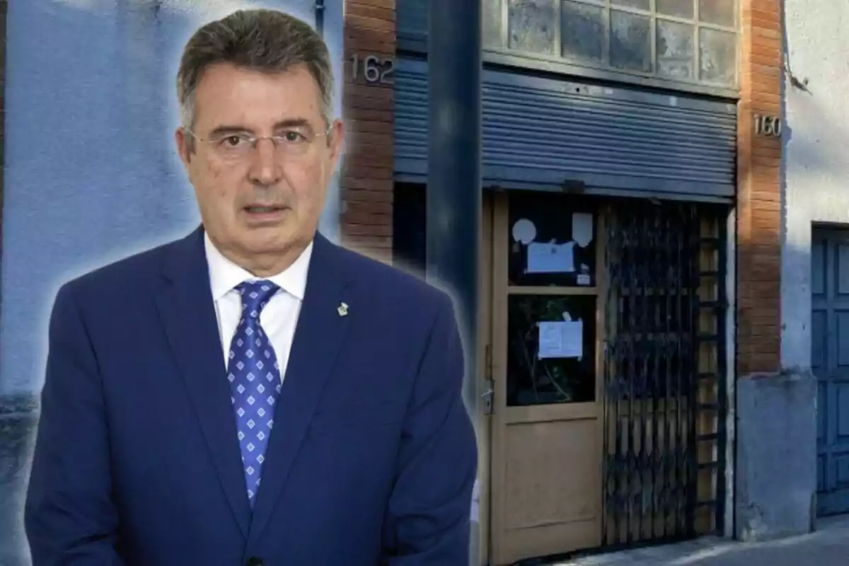 A man in a blue suit and tie standing in front of a building with a metal door and upper windows.