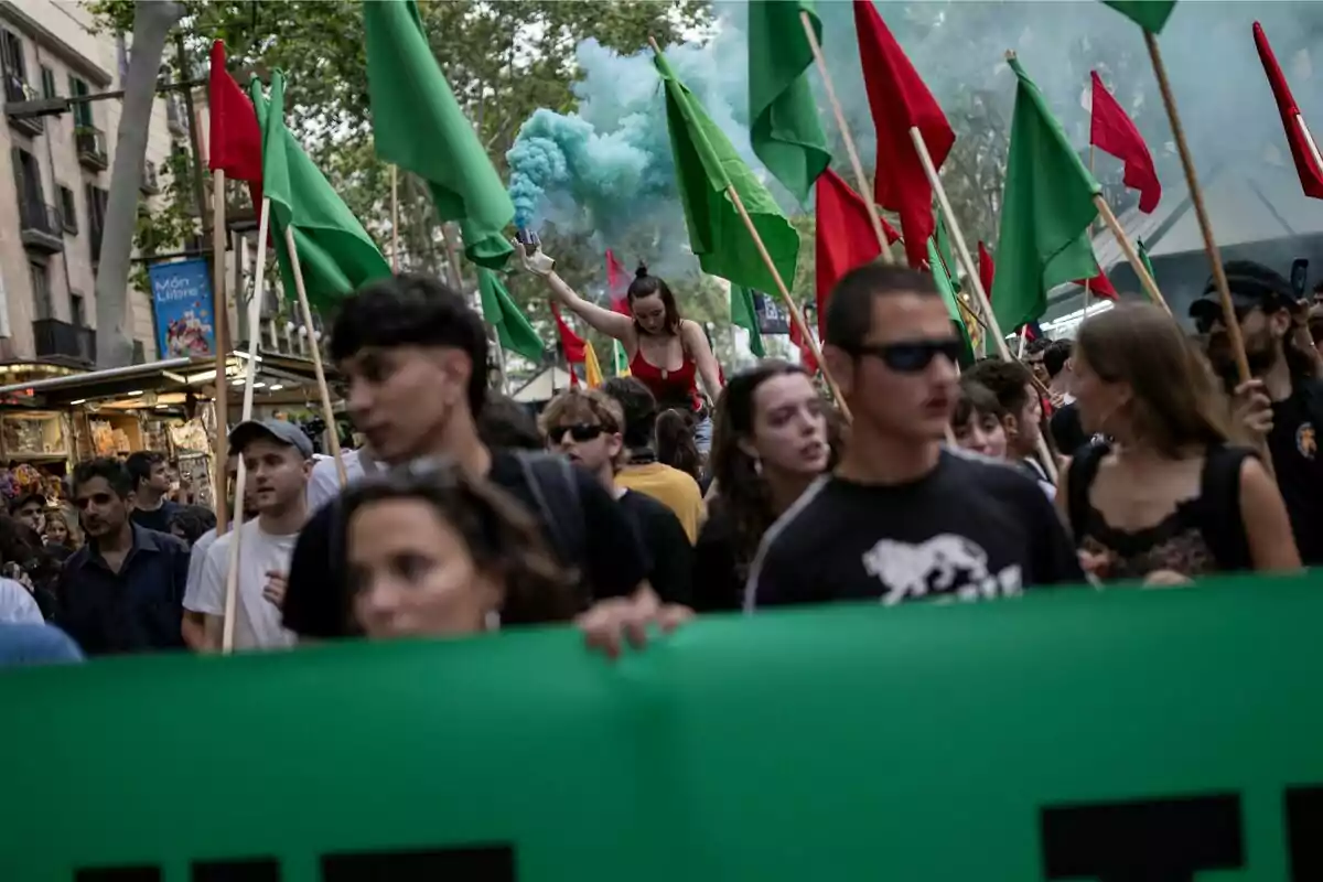 Una multitud de persones marxant amb banderes verdes i vermelles, mentre una dona sosté una bengala de fum blau.