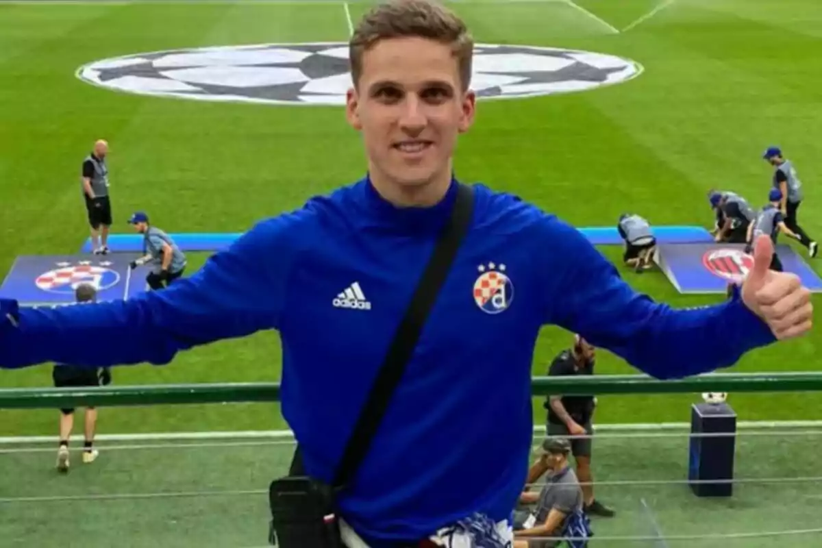 Jakiv Jelkic in a blue Dinamo Zagreb sweatjersey is in a football stadium with the UEFA Champions League logo on the grass.