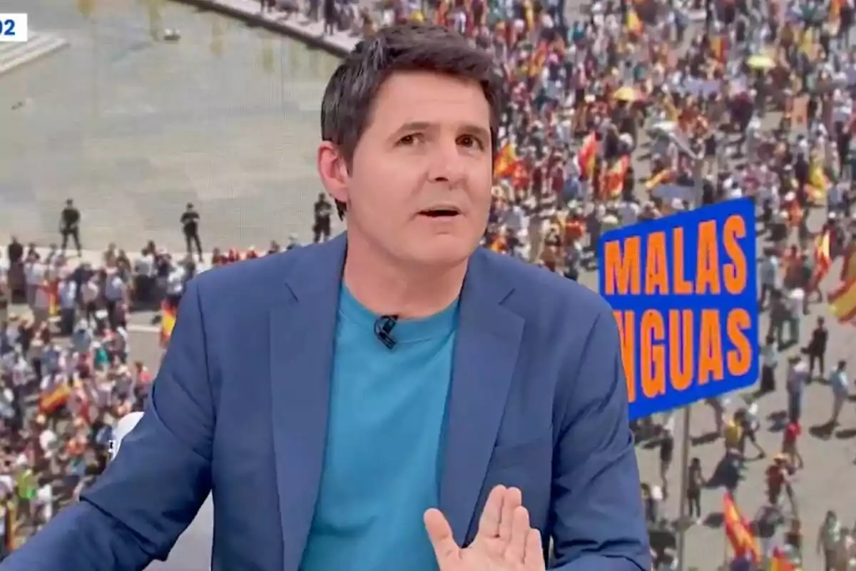 Jesús Cintora amb jaqueta blava i samarreta turquesa està parlant davant d'una multitud en una manifestació, amb un cartell que diu "Males Llengües" al fons.