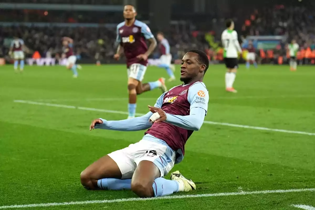 A soccer player celebrates by sliding on his knees on the field as his teammates run towards him.