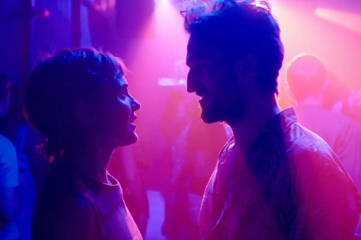 Joan Amargós i Verónica Echegui es miren de prop i somriuen en una discoteca il·luminada amb llums de colors porpra i rosa a A Muerte.