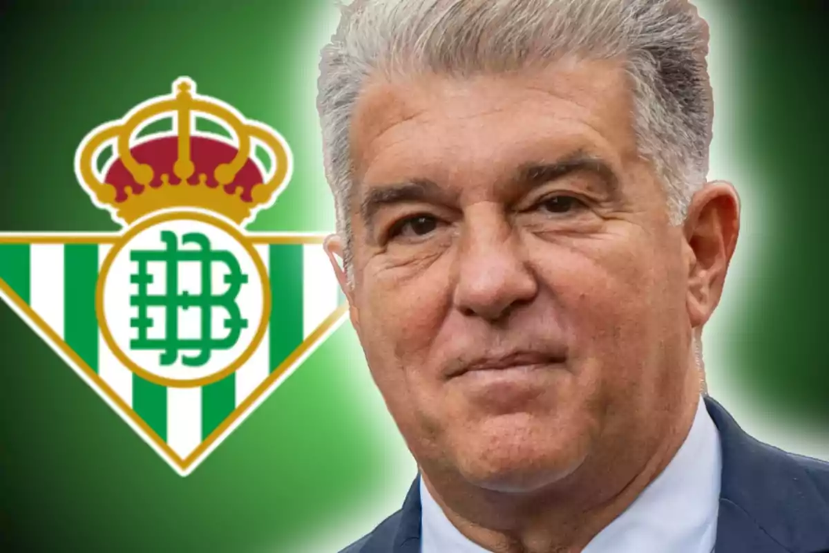 Un home de cabells canosos amb vestit davant de l'escut del Reial Betis.