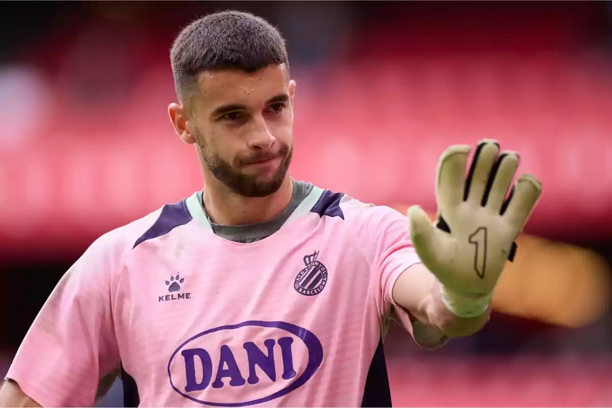 A player in a pink uniform and gloves raises his hand in greeting. A player in a pink uniform and gloves raises his hand in greeting.